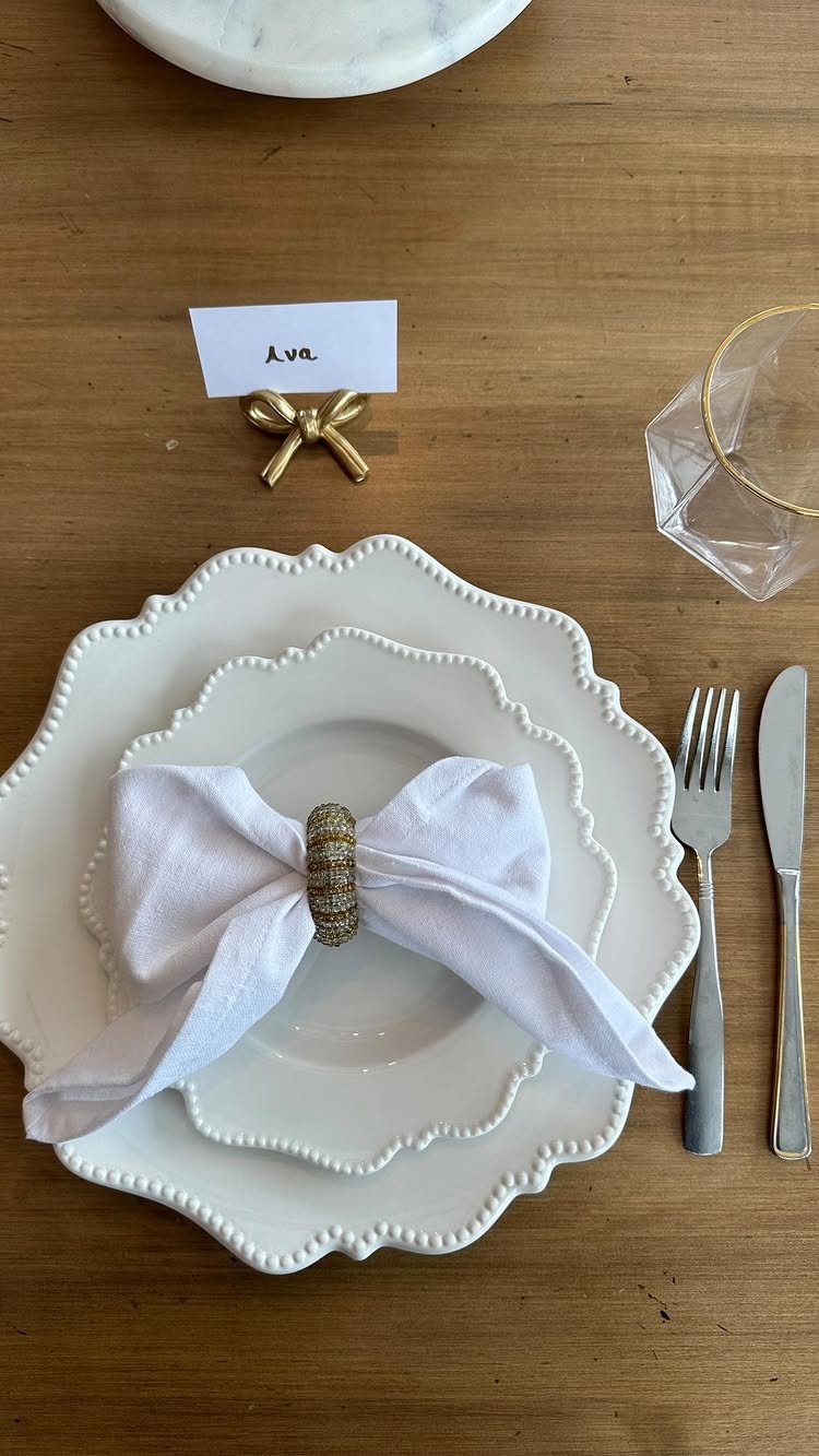 Gold bow-shaped place card holder on a wooden table with white plates.