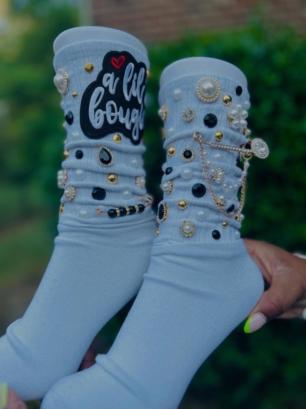 White socks embellished with pearls, rhinestones, and a decorative text patch.