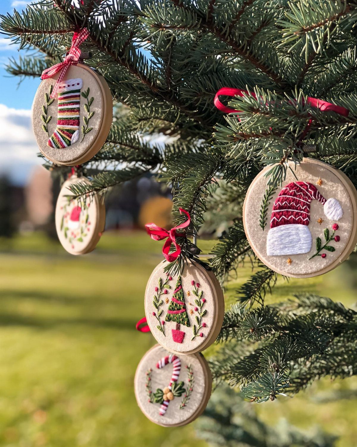 Circular embroidery hoop ornaments with Christmas designs hanging on a green pine tree