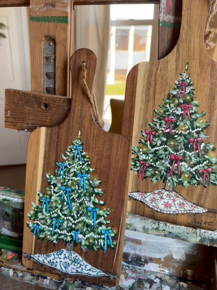 Two wooden cutting boards painted with festive Christmas trees and colorful bows.