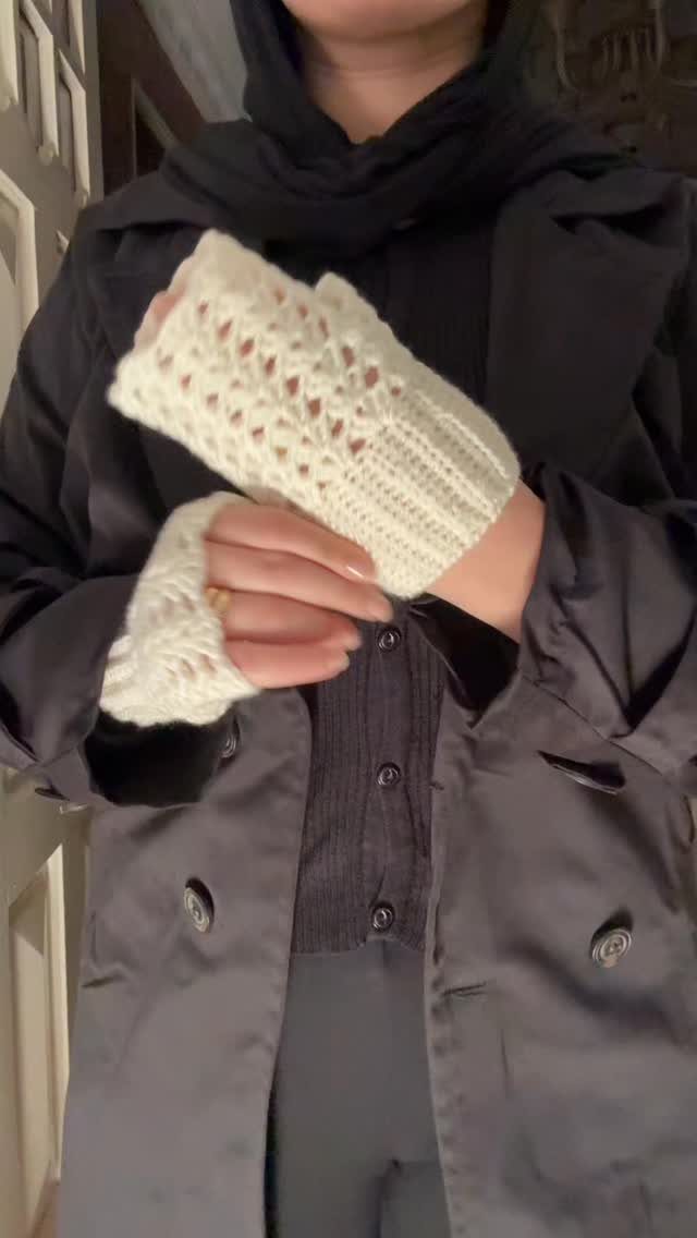 White crocheted fingerless gloves worn by a person in a black coat.