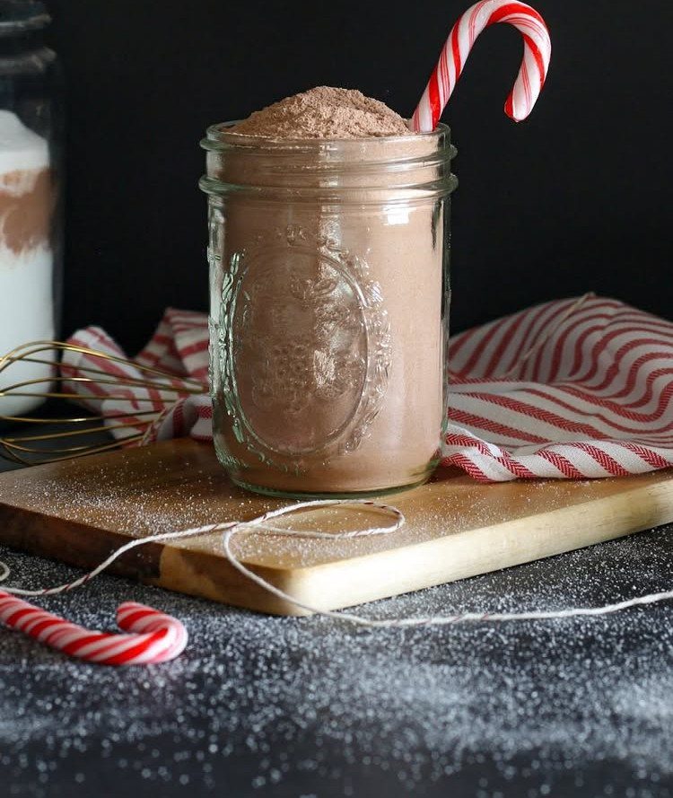 Mason jar filled with hot chocolate mix and a candy cane on wood.
