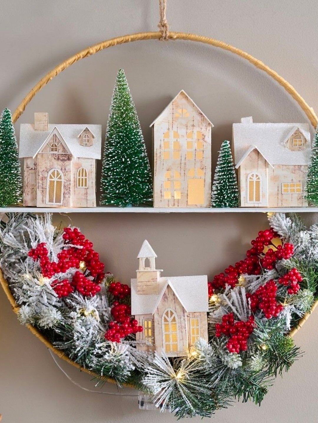 Miniature Christmas village with white houses and trees arranged in a gold hoop wreath