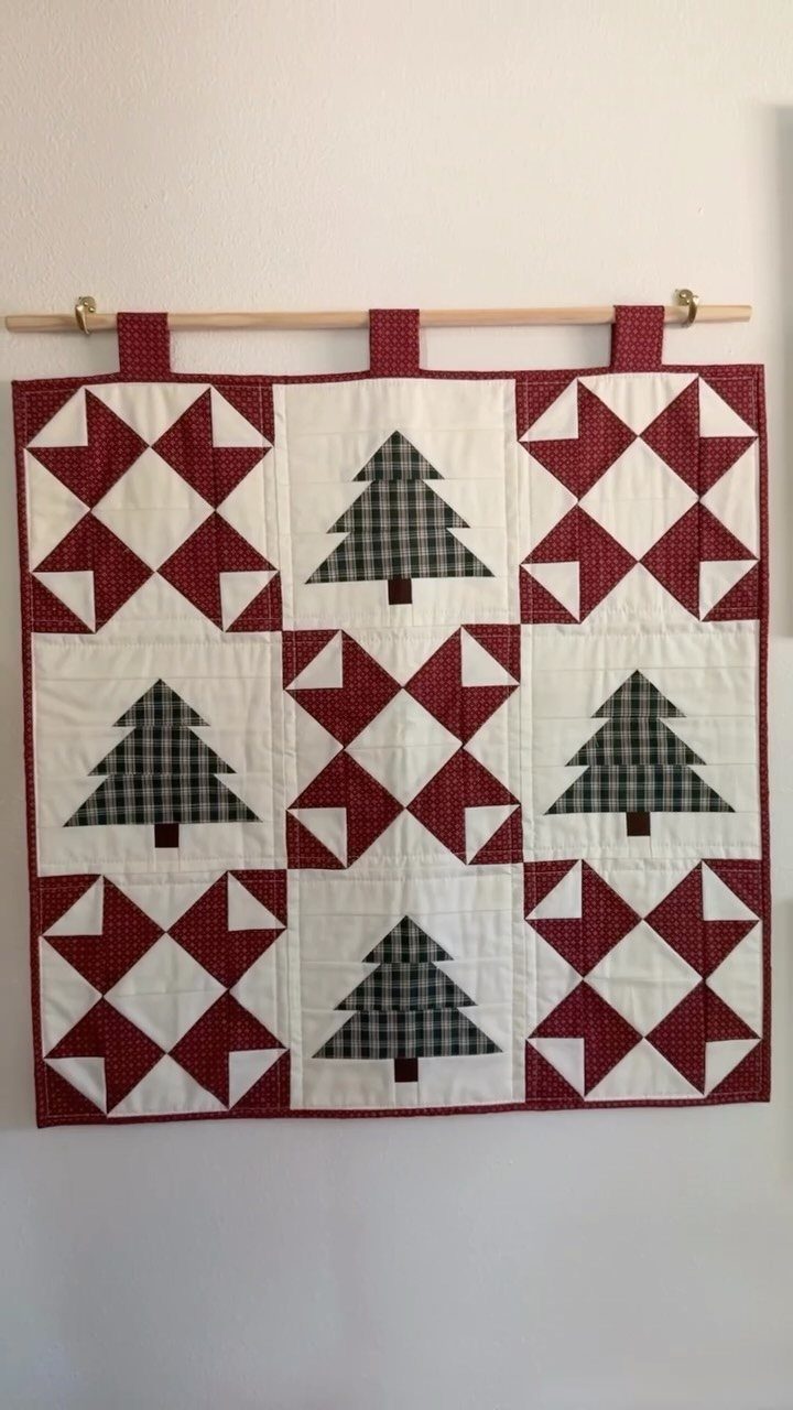 Handmade Christmas quilt with red geometric patterns and green plaid trees hanging on wall