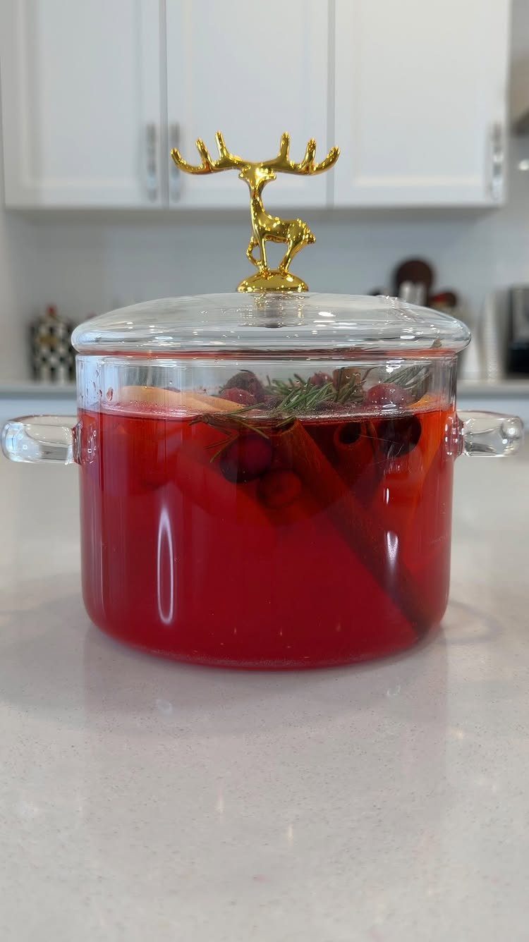 Glass pot of red stovetop potpourri with cinnamon and citrus and gold reindeer lid