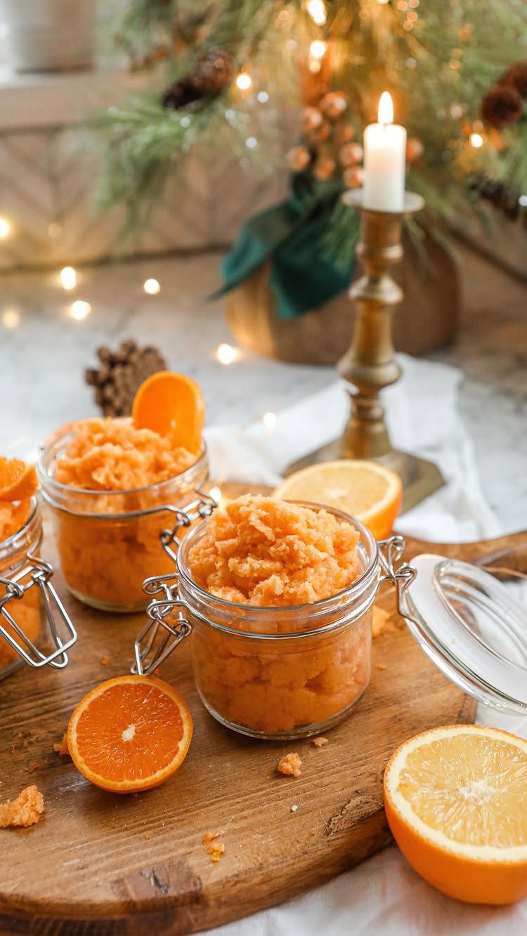 Orange sugar scrub in glass jars on a wooden board with citrus slices.