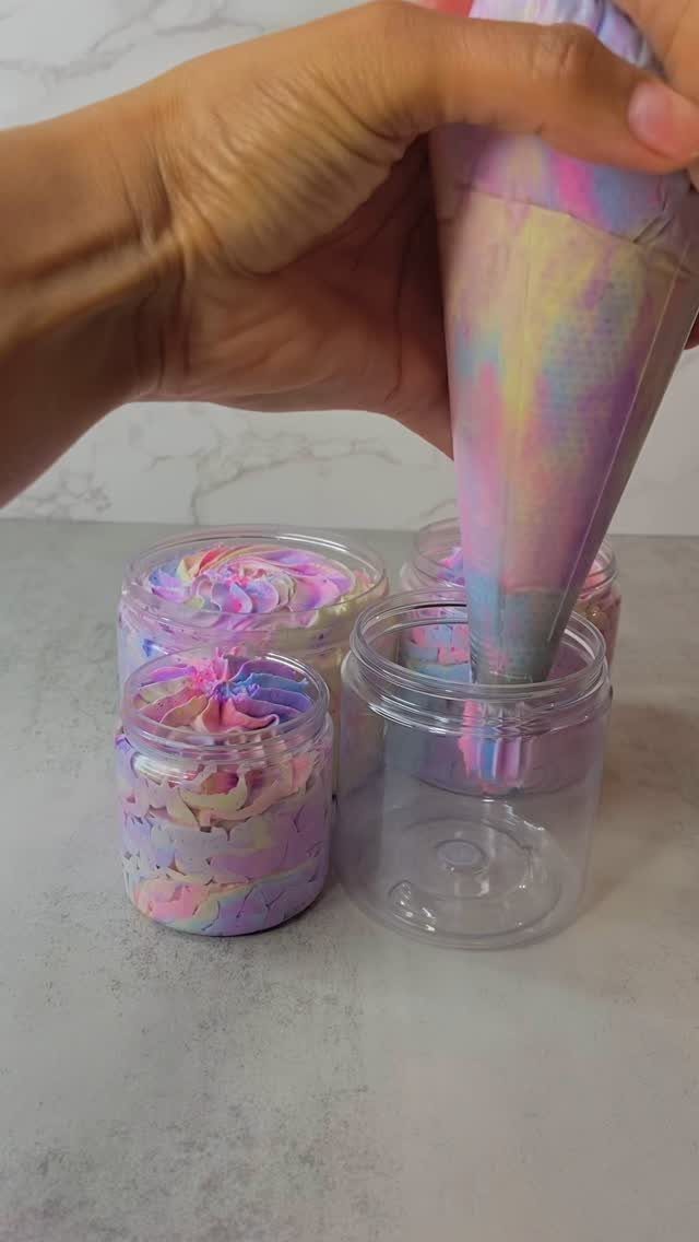 Pastel swirled whipped body butter being piped into small clear plastic jars.