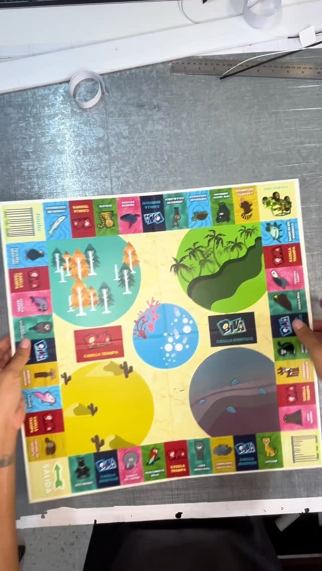 Handmade colorful board game with illustrated zones held by two hands on a desk