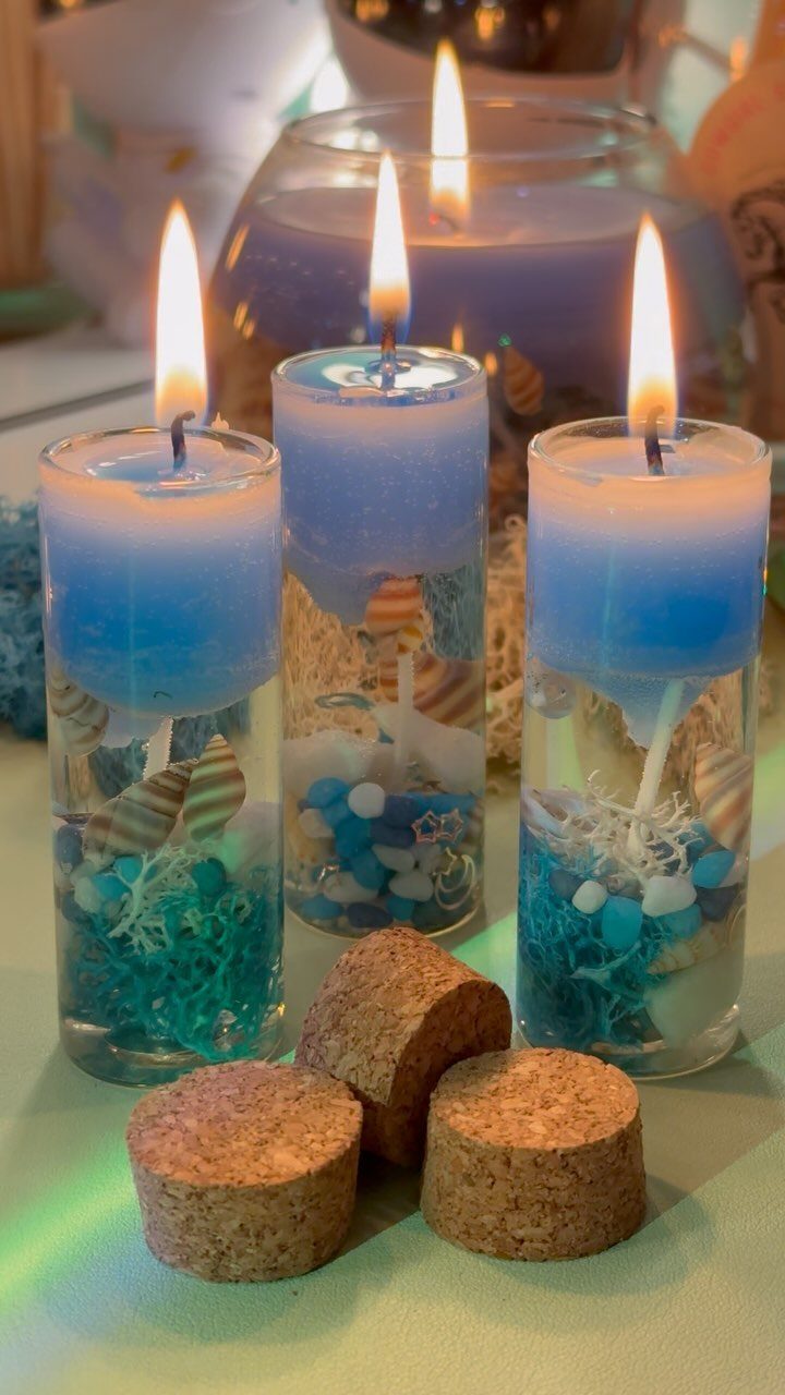 Blue candles in glass cylinders with shells and sand, lit with warm flames.