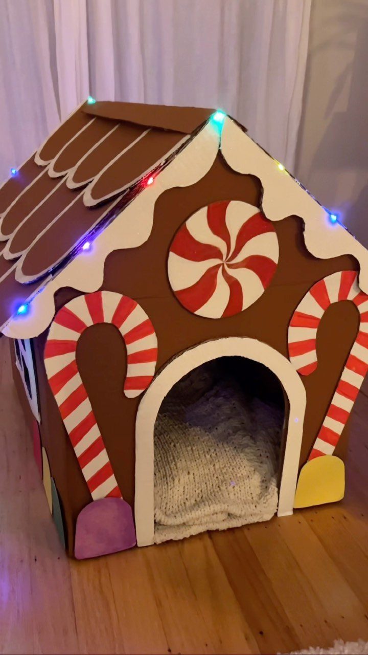 Gingerbread house shaped pet bed with candy decorations and colorful string lights.