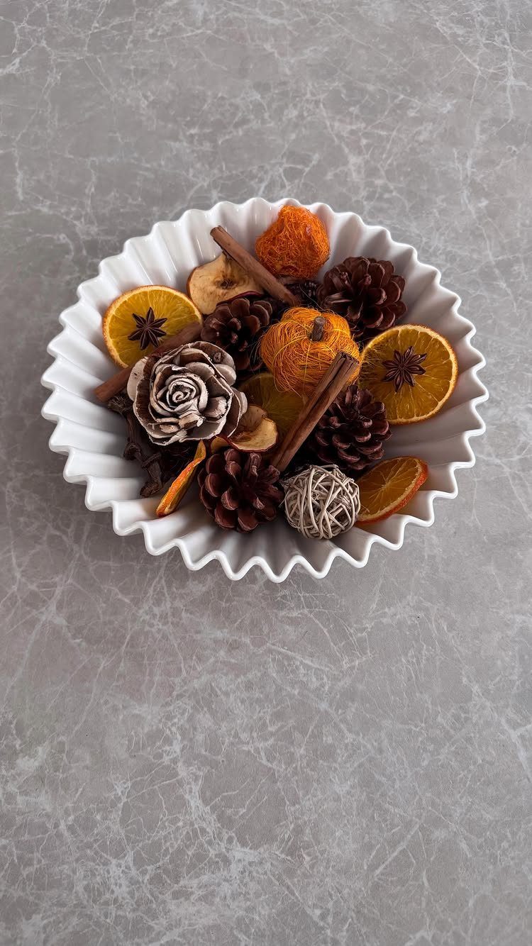 Potpourri with dried oranges, cinnamon, and pinecones in a white fluted bowl.