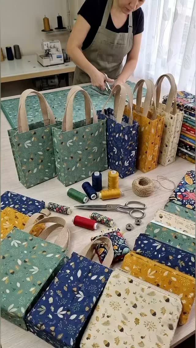 Small leaf-patterned fabric tote bags and sewing supplies on a craft table.