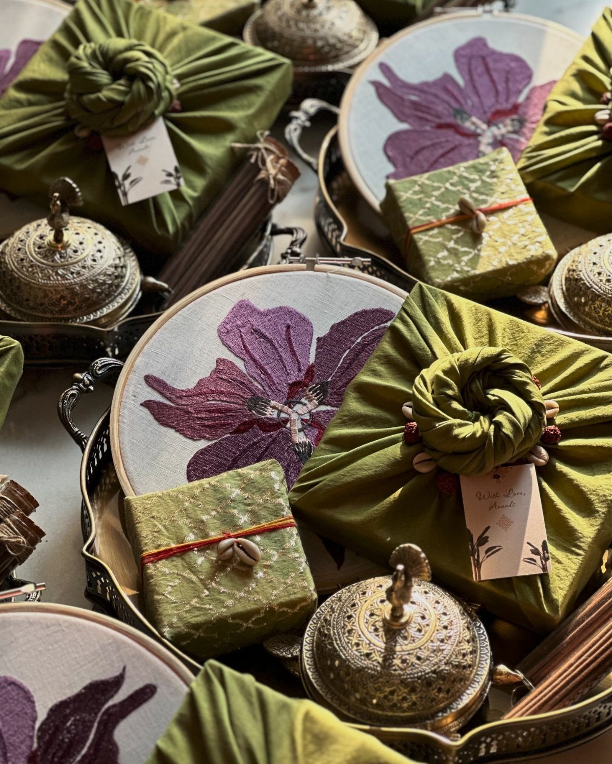 Olive green fabric wrapped gifts with knots and embroidered floral hoops on a tray