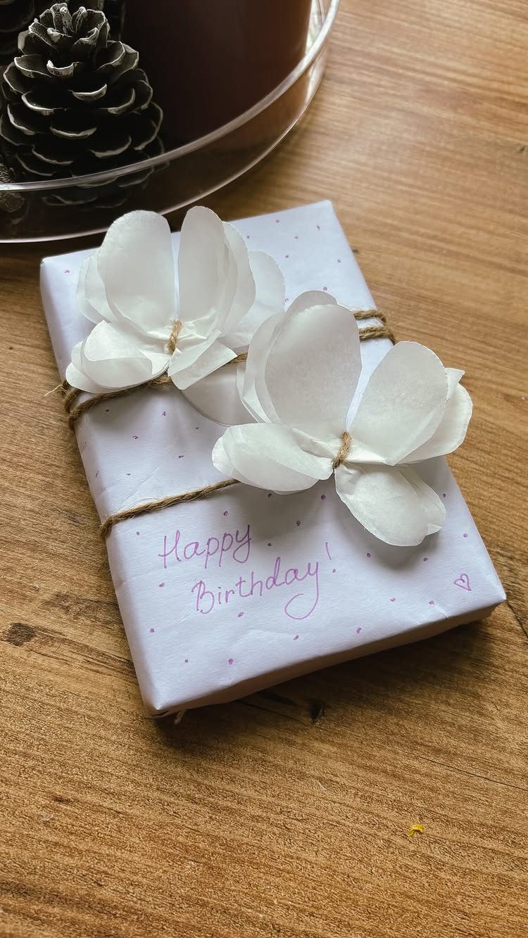 White wrapped gift with pink dots and tissue paper flowers tied with twine.