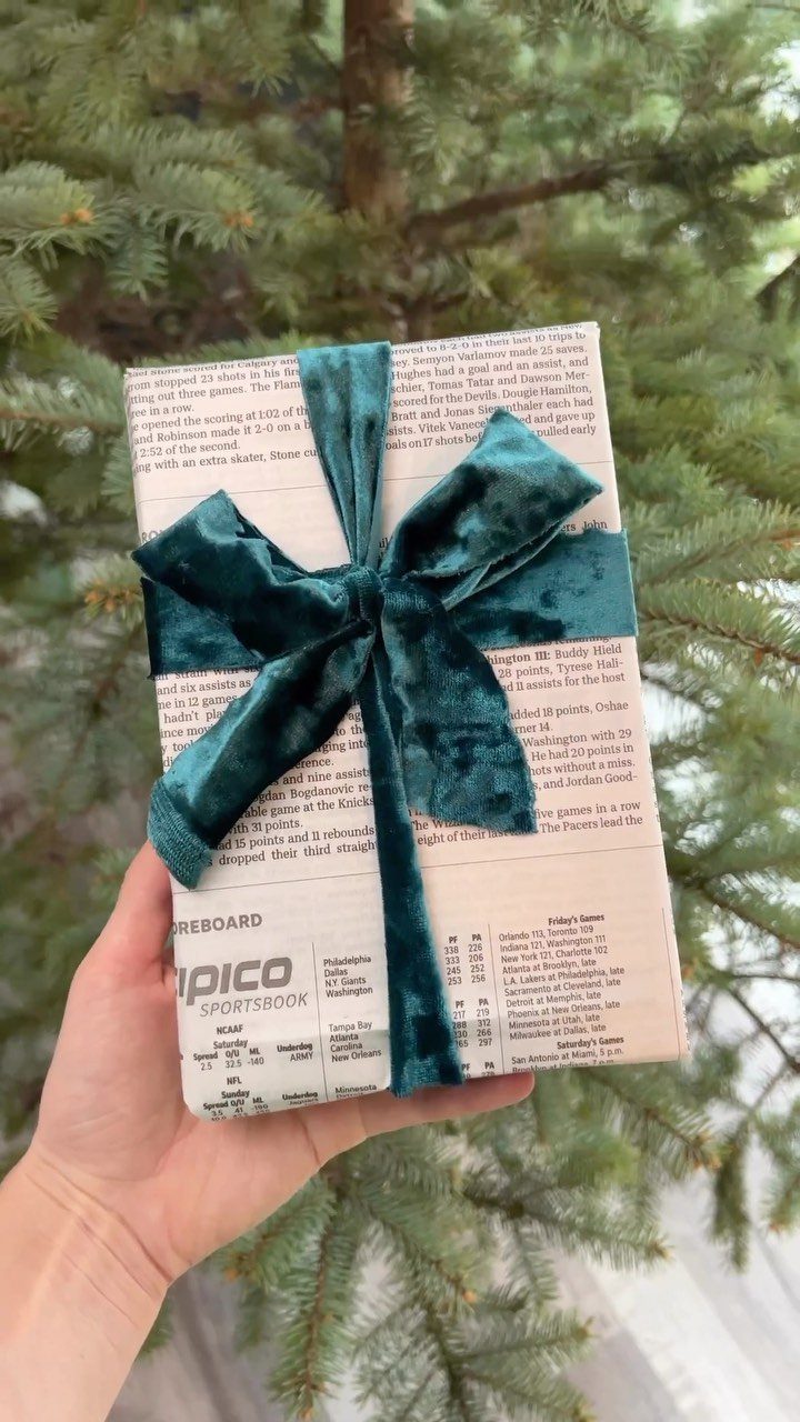 Gift wrapped in newspaper print paper with a large teal velvet bow.