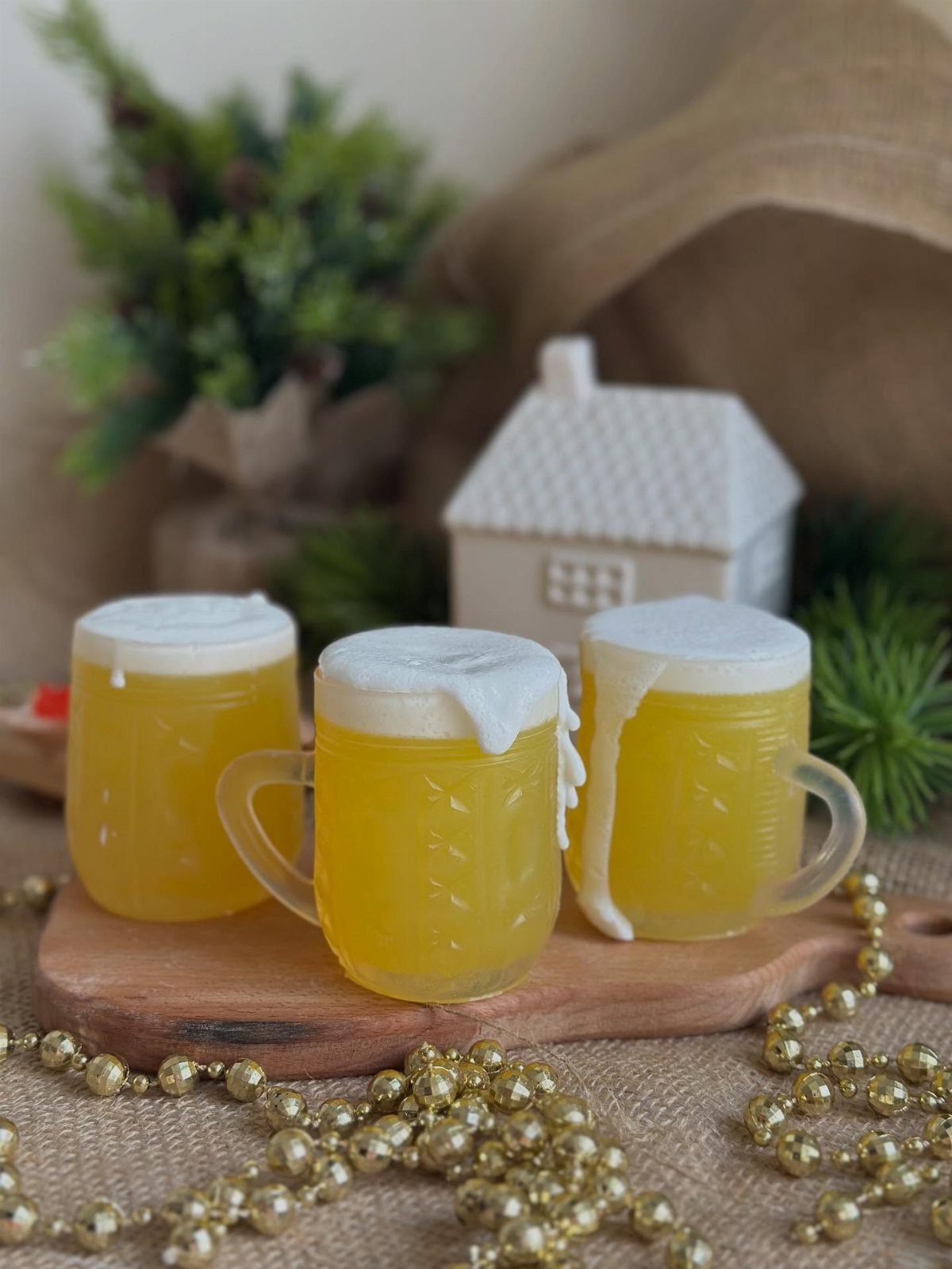 Three yellow beer-mug-shaped soaps with white foam on a wooden board.