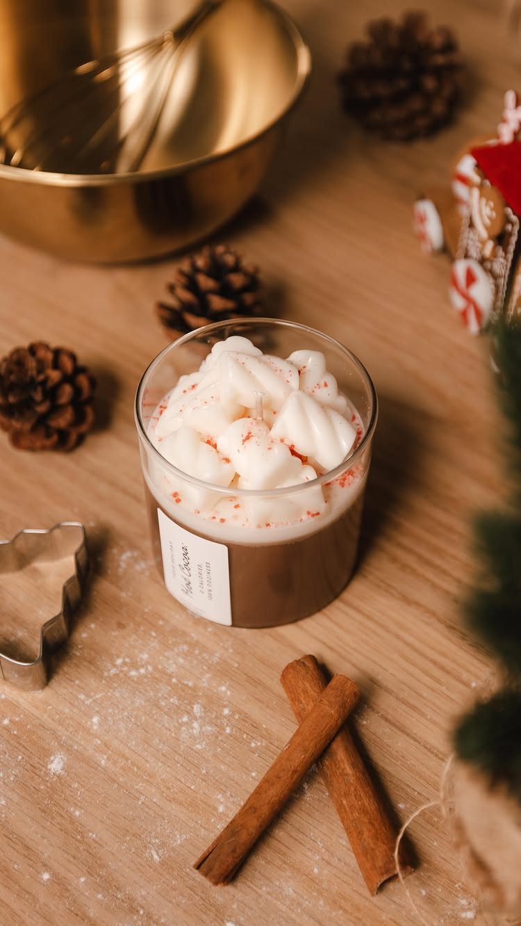Brown dessert-style candle with whipped wax topping on a wooden table with cinnamon.