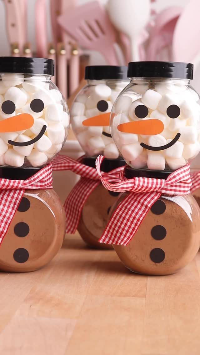 Three snowman-themed glass jars filled with hot cocoa powder and white marshmallows.