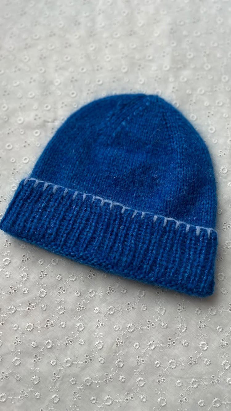 Royal blue knitted beanie with a ribbed cuff on white patterned fabric.