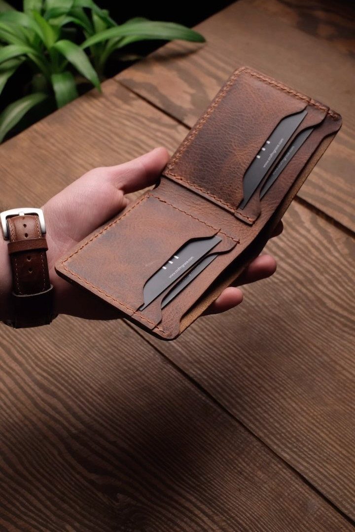 Handmade brown leather wallet held open over a rustic wooden table background