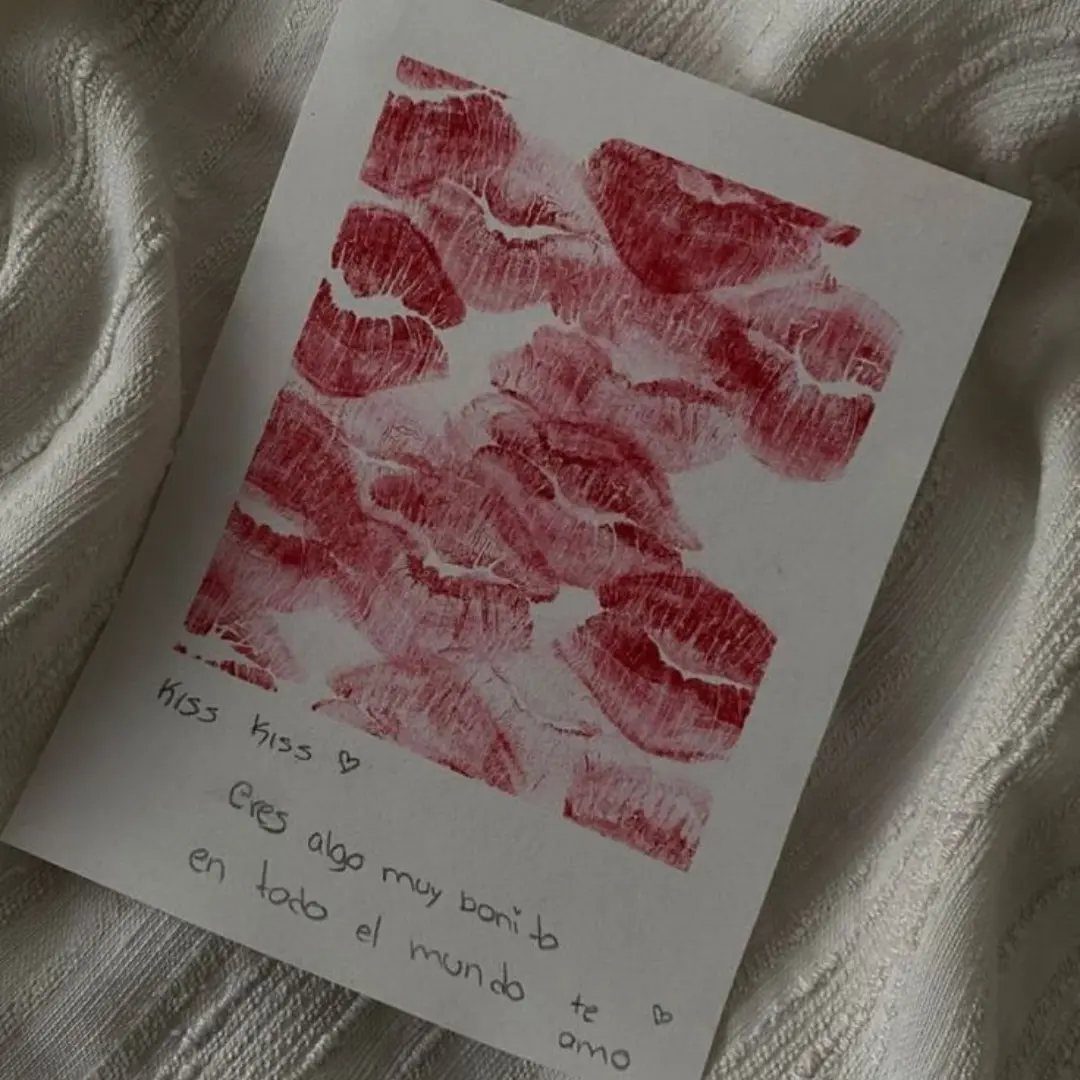 Red lipstick kiss prints and handwritten Spanish love note on white paper.