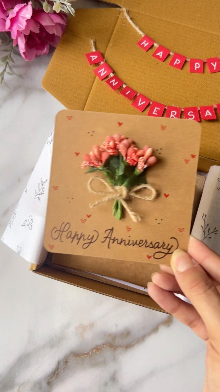 Hand holding a small anniversary card with a miniature flower bouquet and twine.