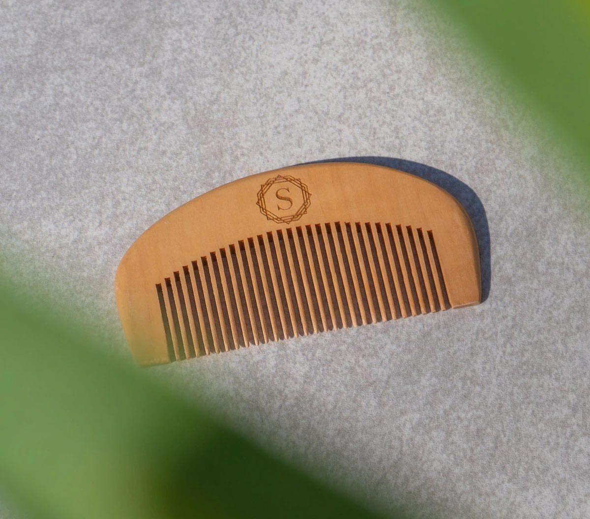 Wooden beard comb with monogrammed S on a grey textured background