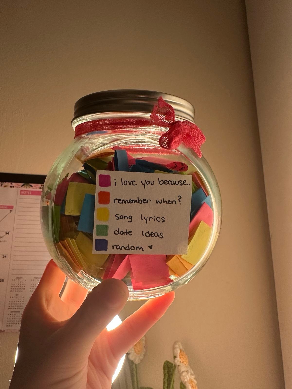 Glass jar filled with colorful handwritten notes and a category label held by hand.