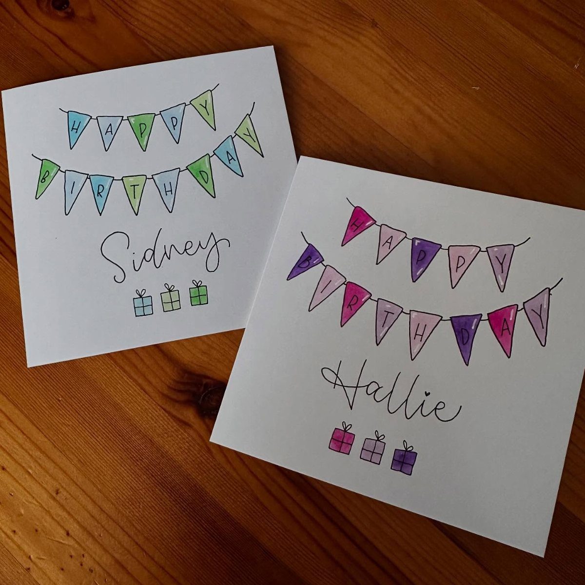 Two handmade birthday cards with colorful bunting flags and cursive names on wood.