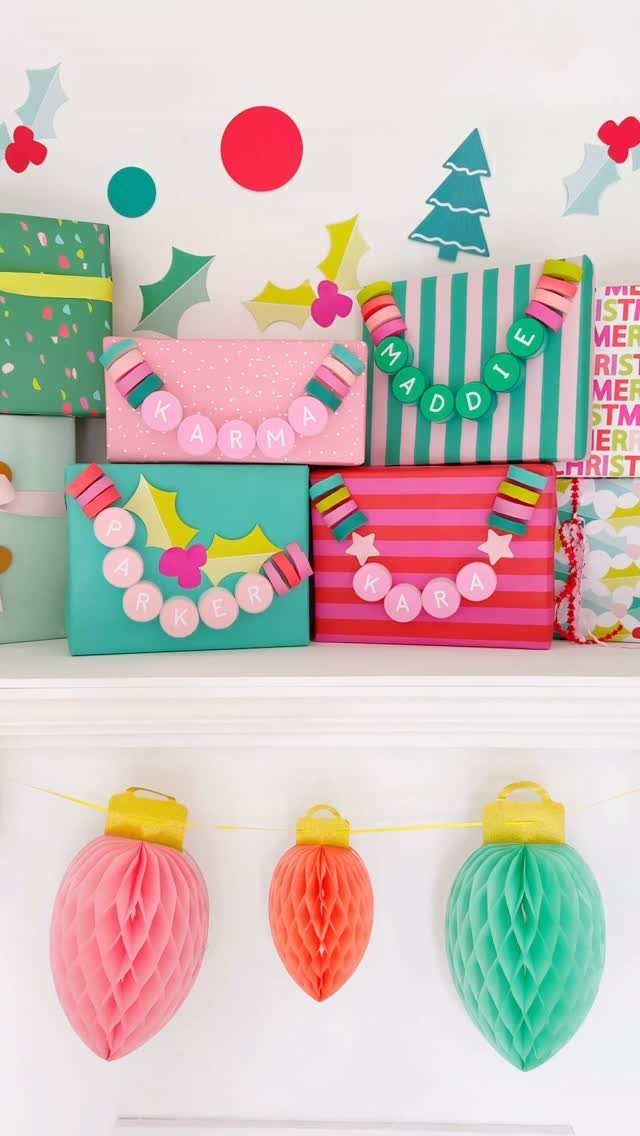 Colorful wrapped holiday gifts decorated with beaded name necklaces on a white shelf