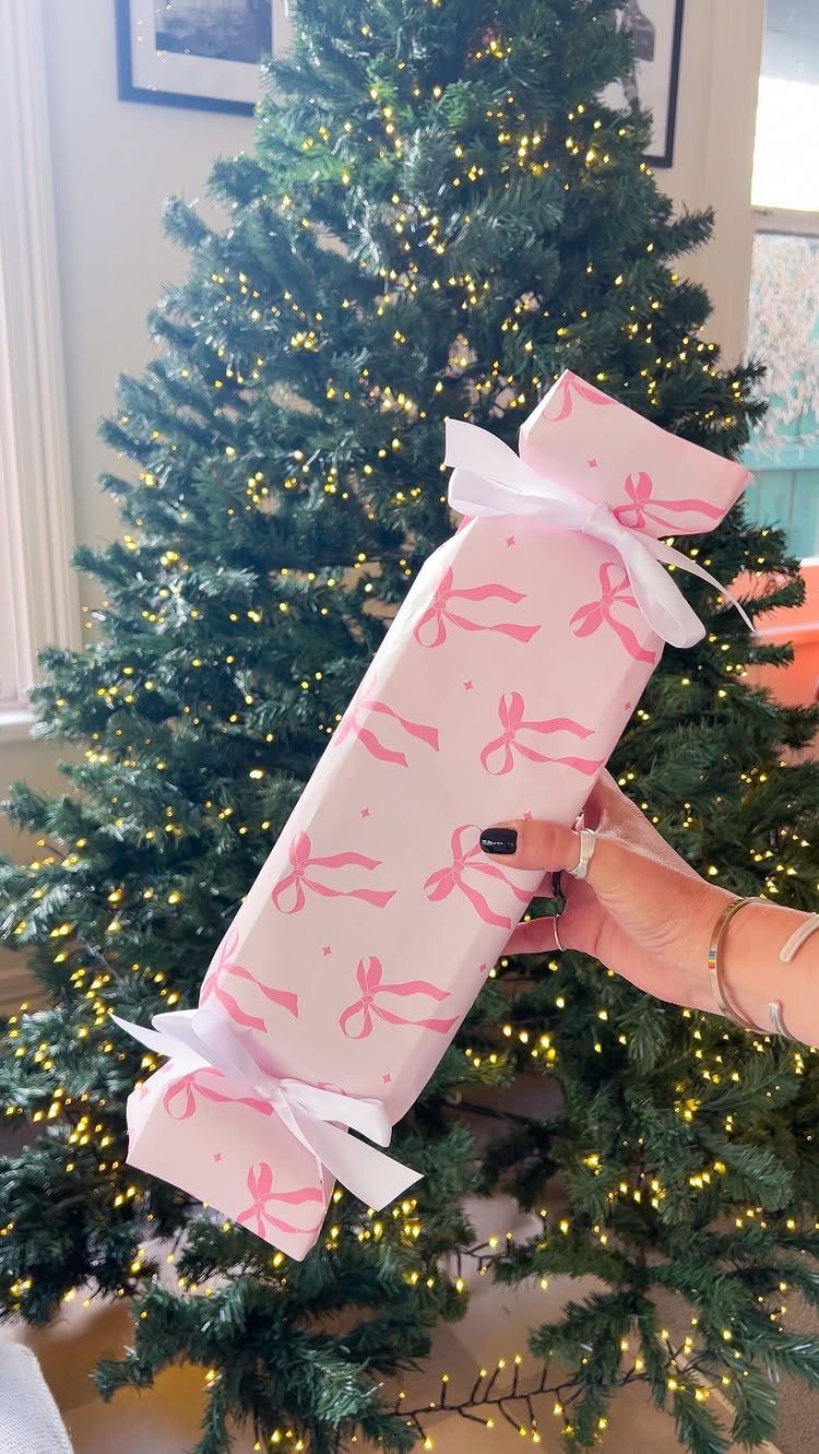 Wrapped gift with pink bow patterns and white ribbons held before a Christmas tree