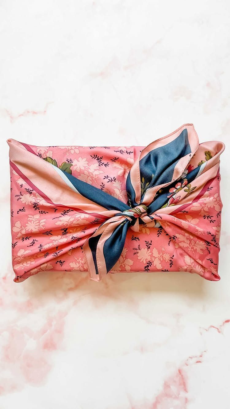 Gift wrapped in pink floral fabric and tied with a blue silk scarf.