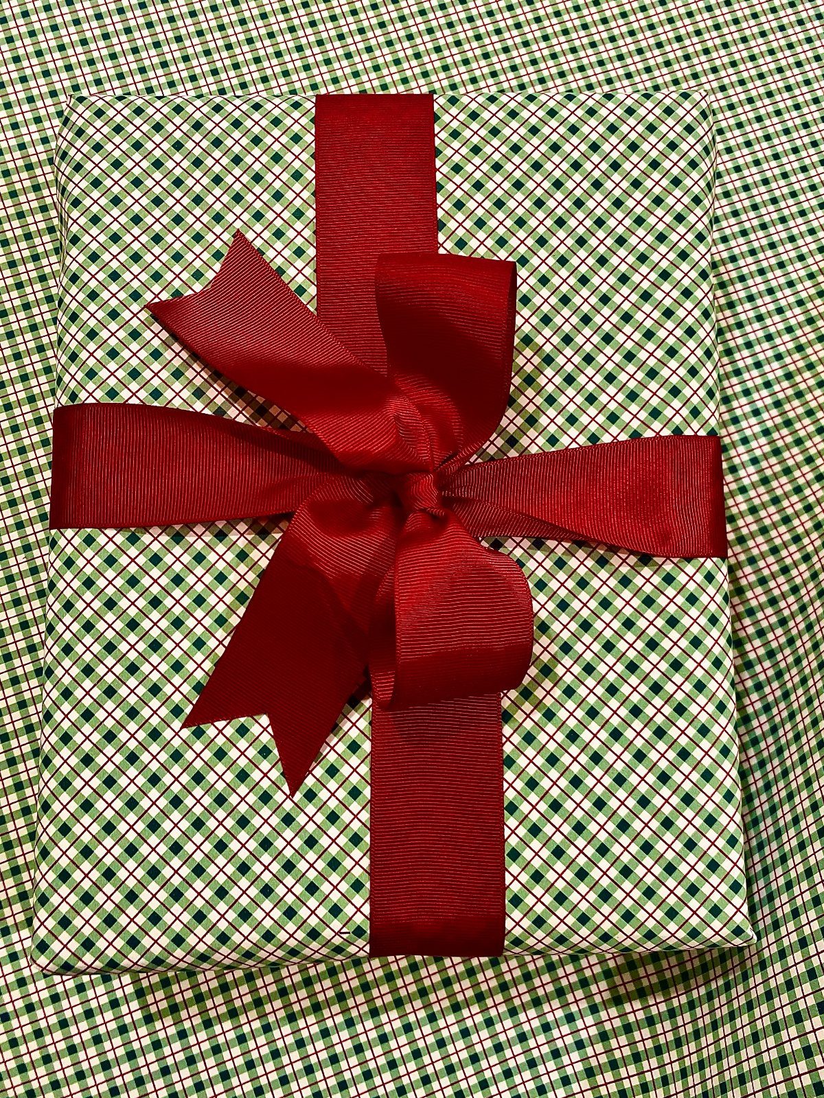 Wrapped gift with green and white checkered paper and a red satin bow.