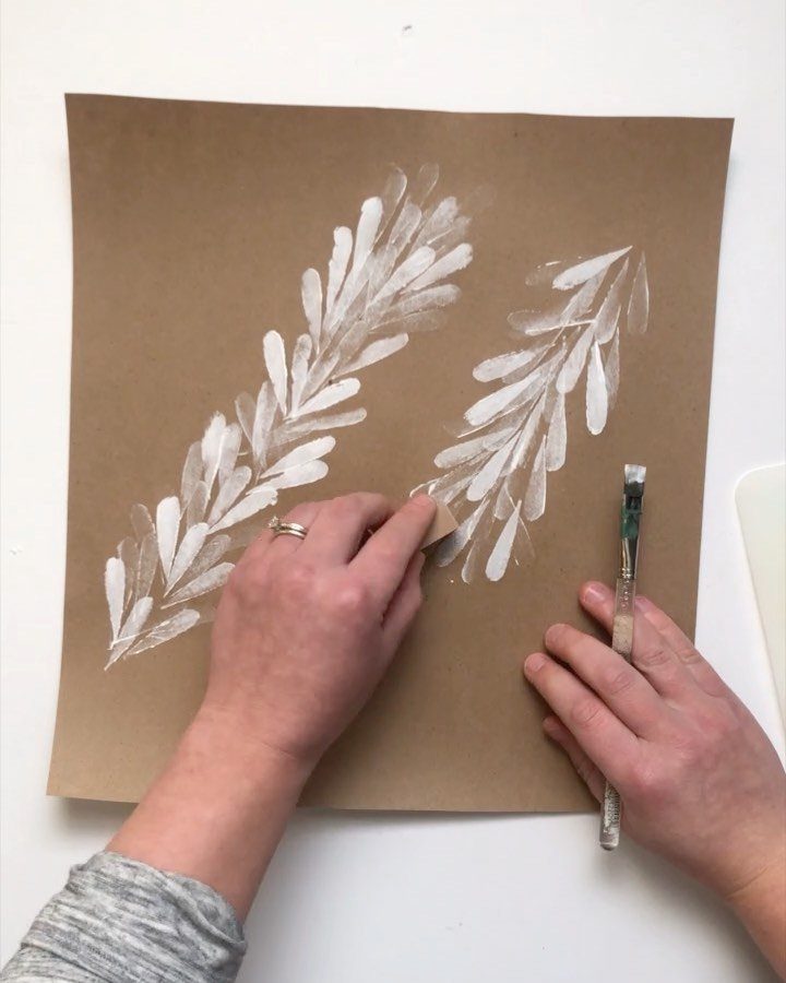 Hands painting white botanical designs on brown kraft wrapping paper with a brush