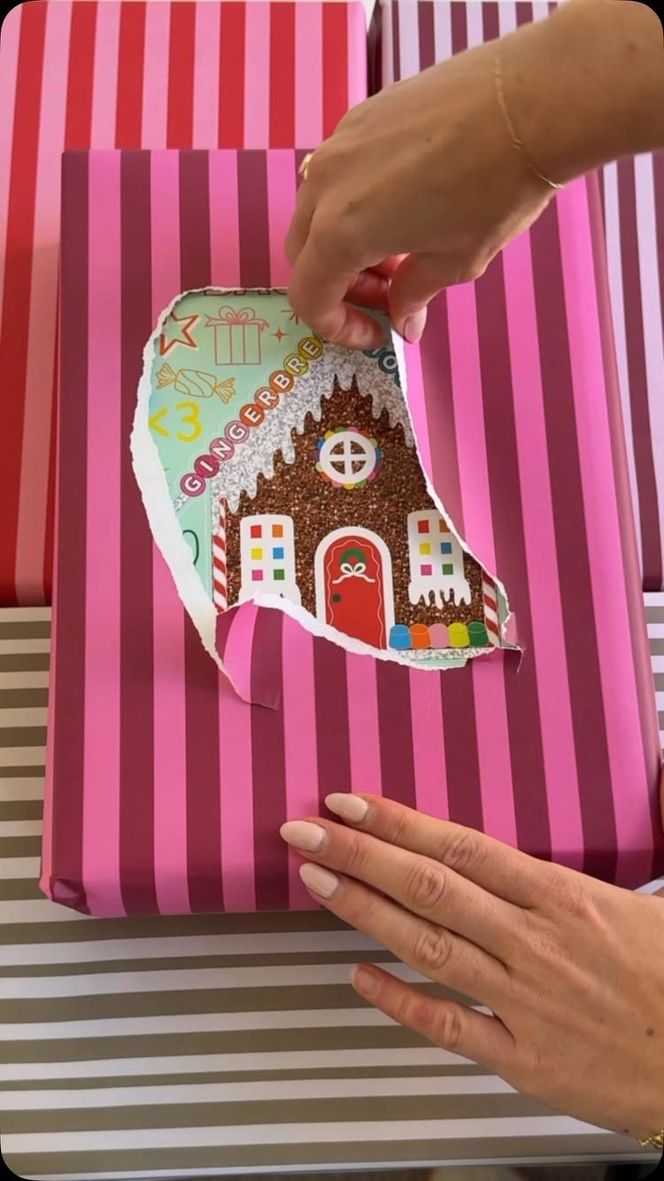 Hands peeling striped pink wrapping paper to reveal a gingerbread house design underneath.
