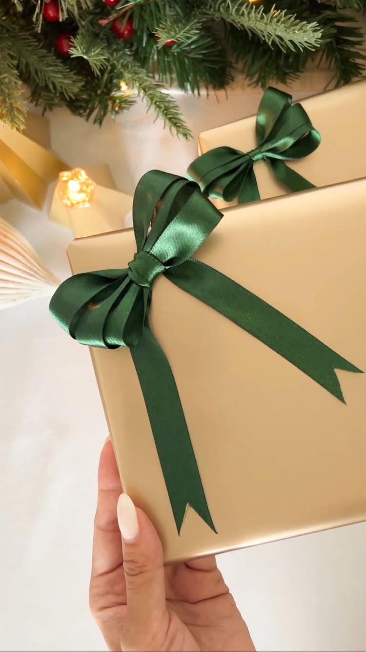 Gold wrapped gift with a dark green satin ribbon held by a hand.
