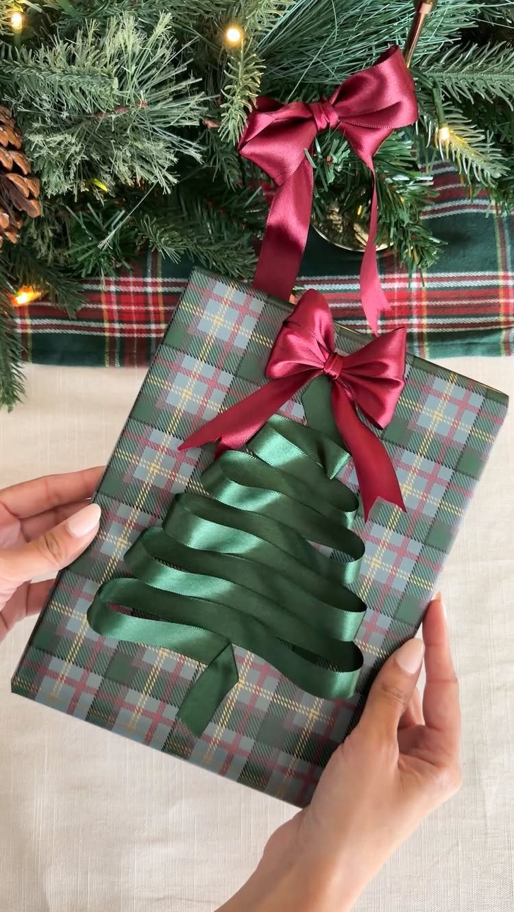 Plaid wrapped gift with a green ribbon Christmas tree and red bow topper.