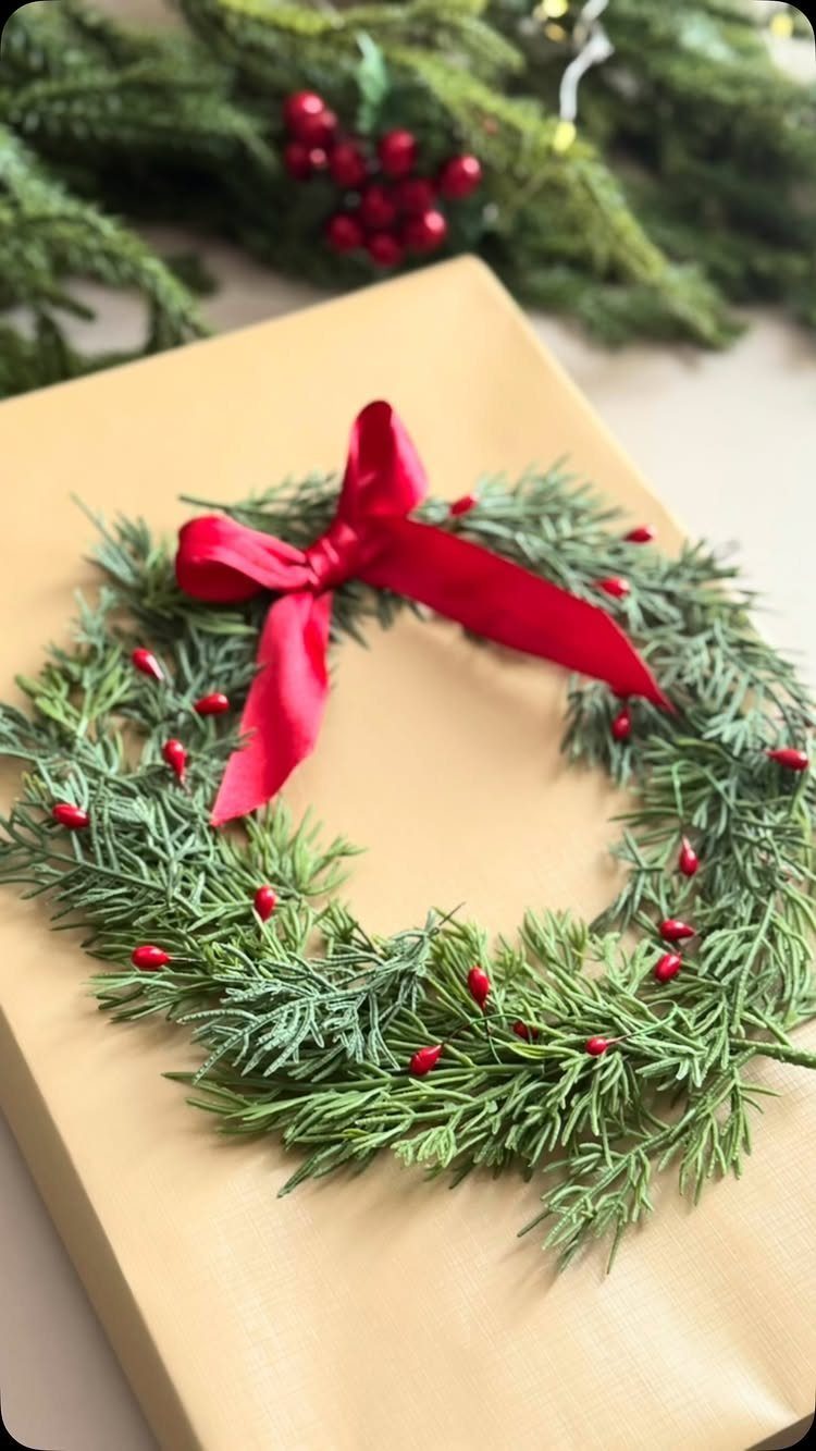 Brown wrapped gift topped with a small evergreen wreath and red satin bow