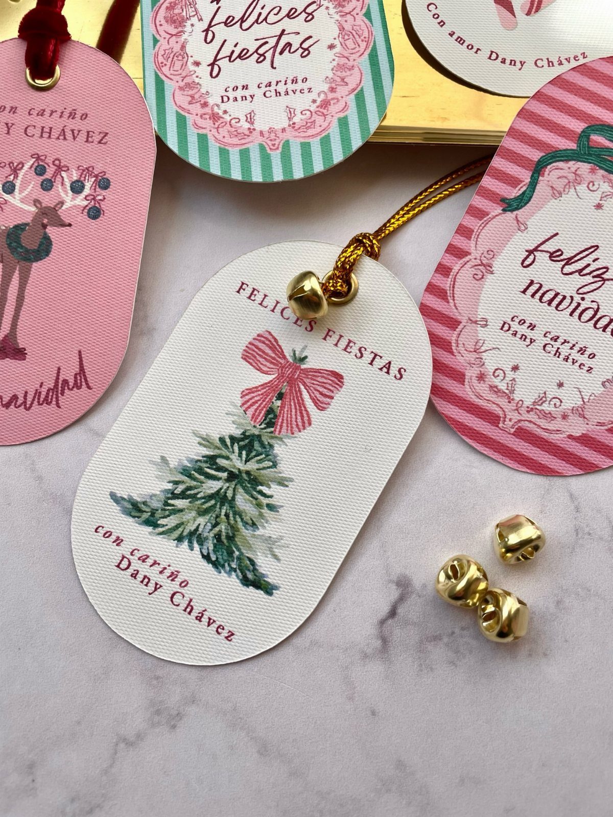 Holiday gift tags with Christmas illustrations and small gold jingle bells on marble.