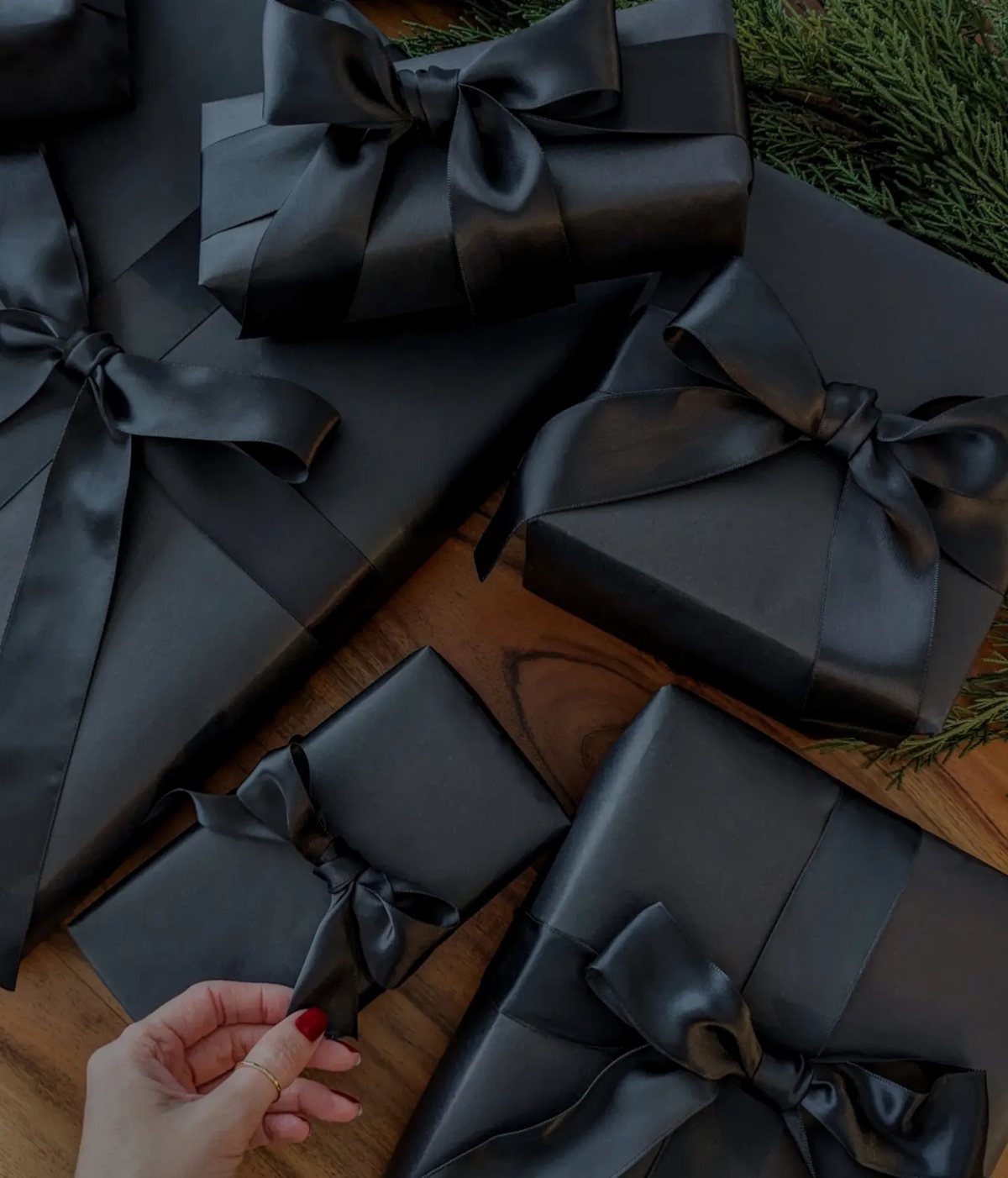 Black wrapped gifts with satin ribbons on a wooden table with evergreen branches
