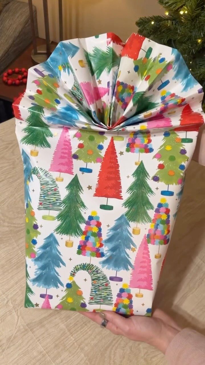 Gift wrapped in colorful watercolor Christmas tree paper with a folded fan top.