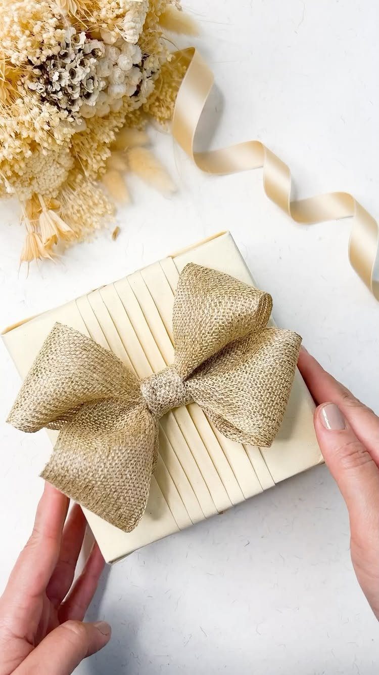 Pleated cream gift wrap with a large gold burlap bow held by hands