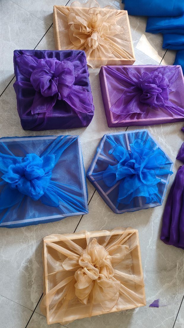 Gift boxes wrapped in sheer purple, blue, and beige fabric with matching bows.