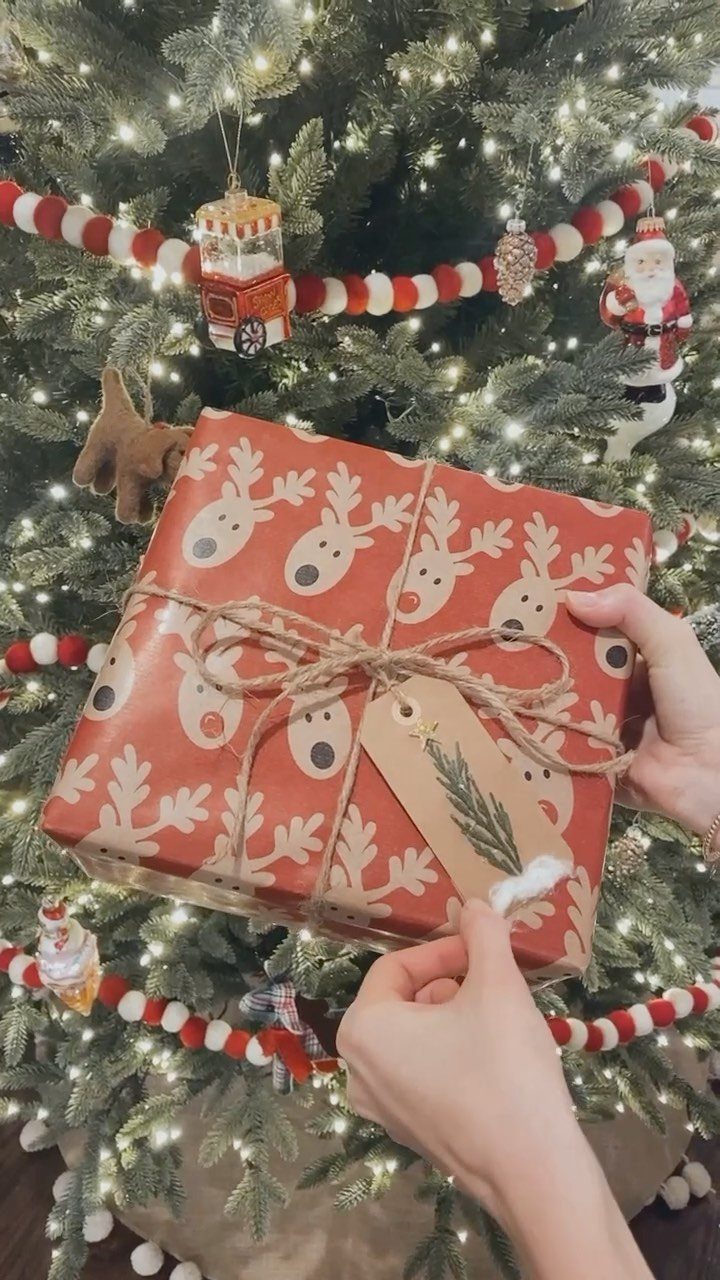 Wrapped gift with reindeer paper and twine held before a decorated Christmas tree
