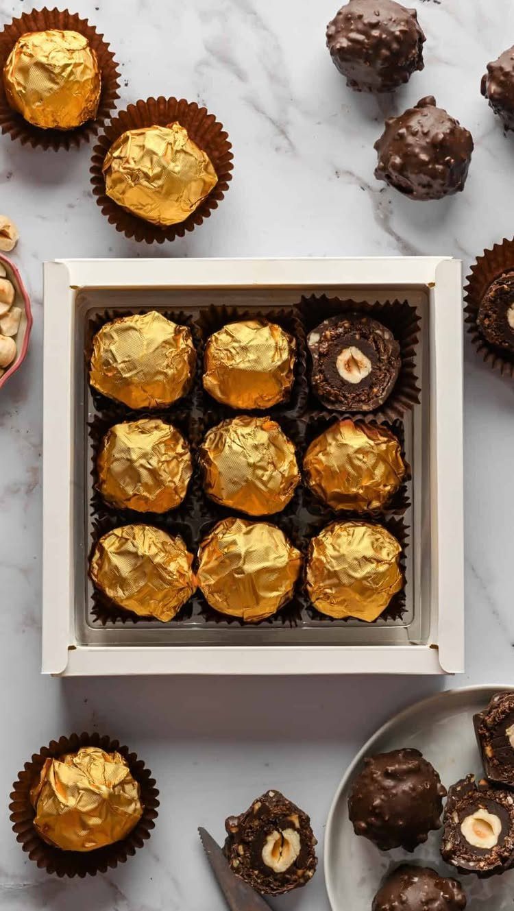 Chocolate hazelnut truffles wrapped in gold foil inside a white gift box.