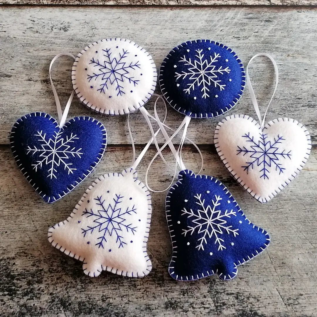 Felt ornaments in blue and white with stitched snowflakes on a wooden background