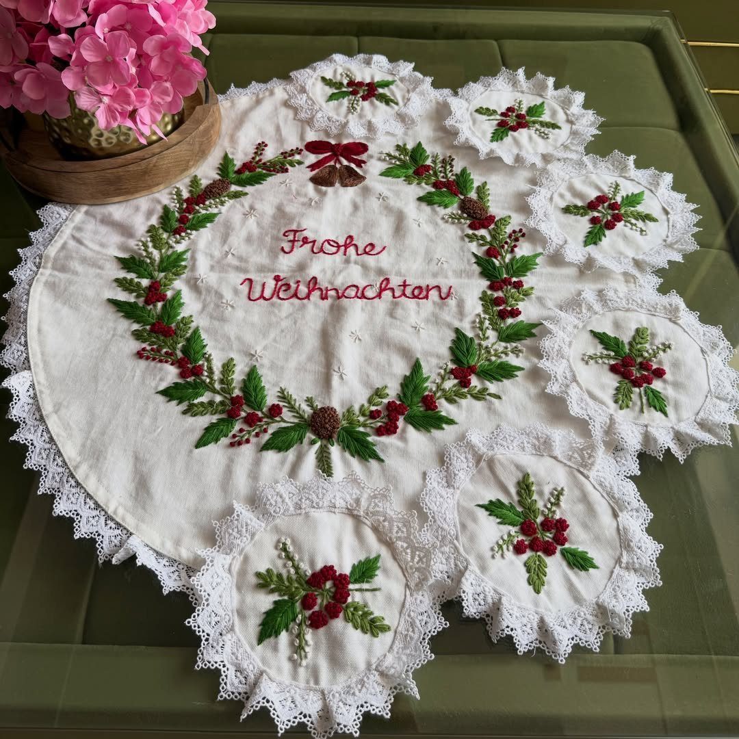 Embroidered white table runner and coasters with Christmas wreaths and red German text.