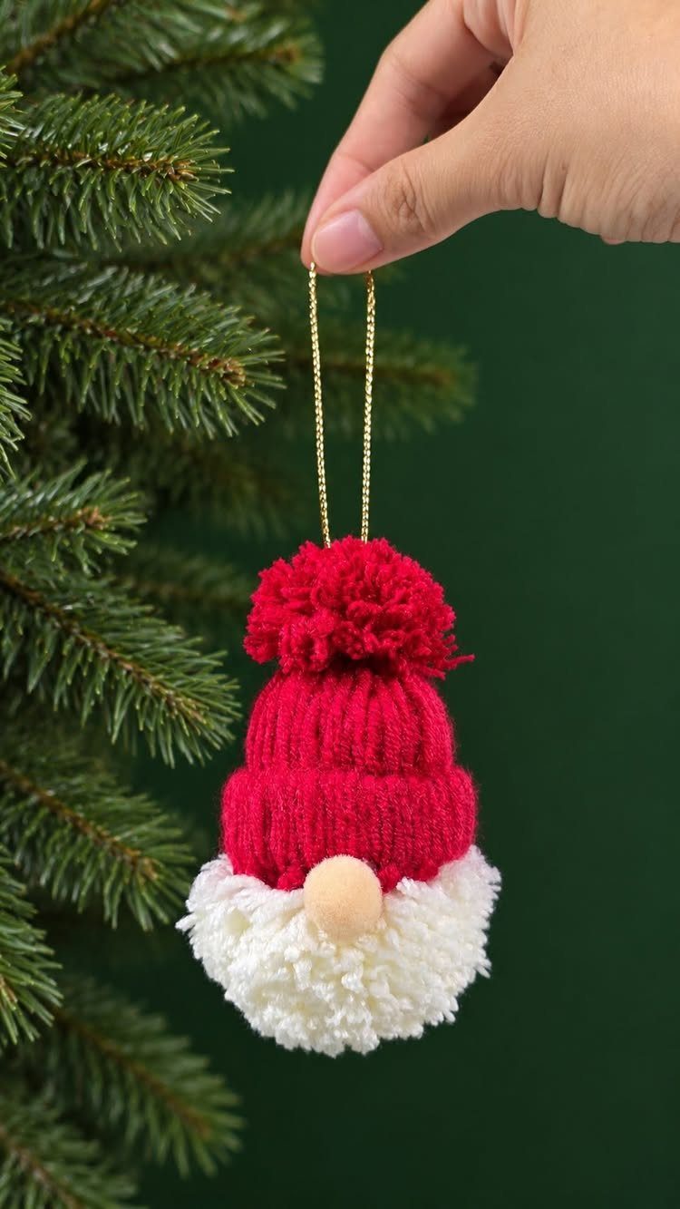 Handmade gnome ornament with red knitted hat and white beard hanging by pine branches.