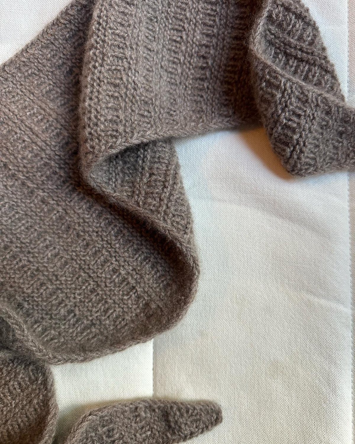 Taupe hand-knitted wool scarf with textured stitch draped on white fabric