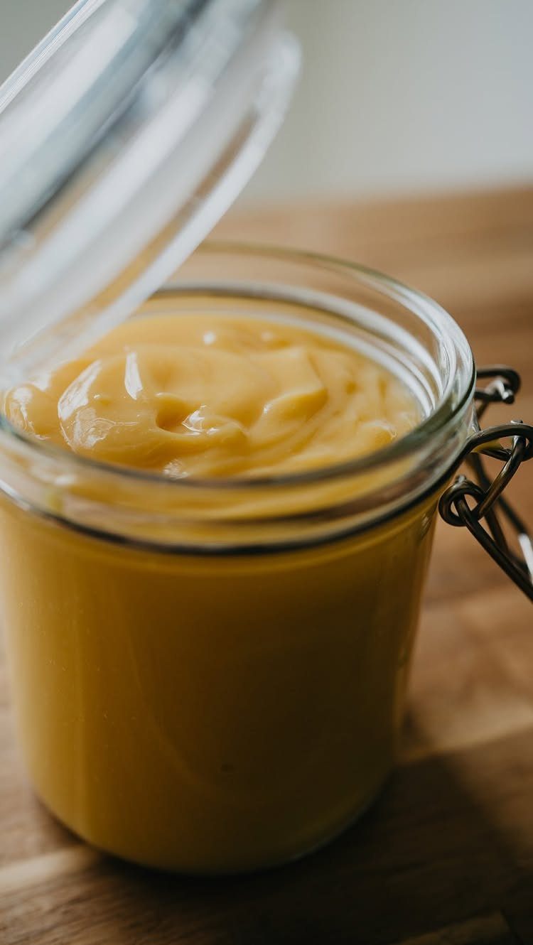 Yellow lemon curd in an open glass jar on a wooden table